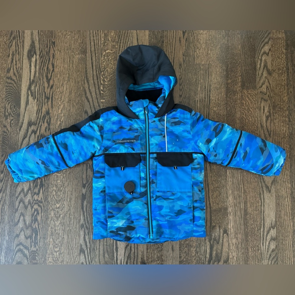 Obermeyer children’s blue camo ski jacket with a black hood and four pockets.